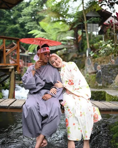 Seorang pengunjung berkimono tradisional Jepang berpose di jembatan melengkung Umbulan Tanaka dengan kolam ikan koi di bawahnya.